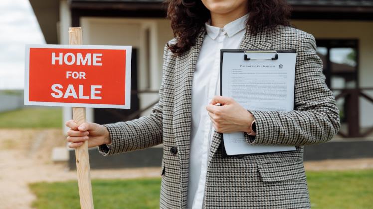a realtor holding a for sale sign